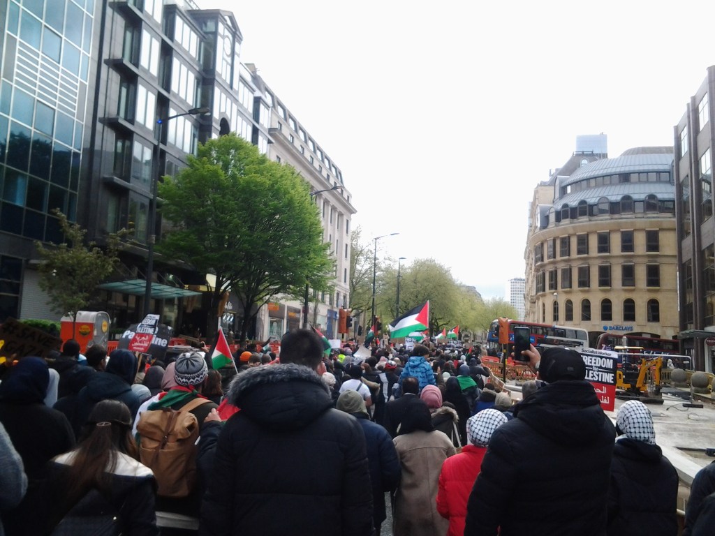 Large crowd of protesters coming into Colmore Row. Signs saying Freedom for Palestine. Barclays bank is in the distance. 