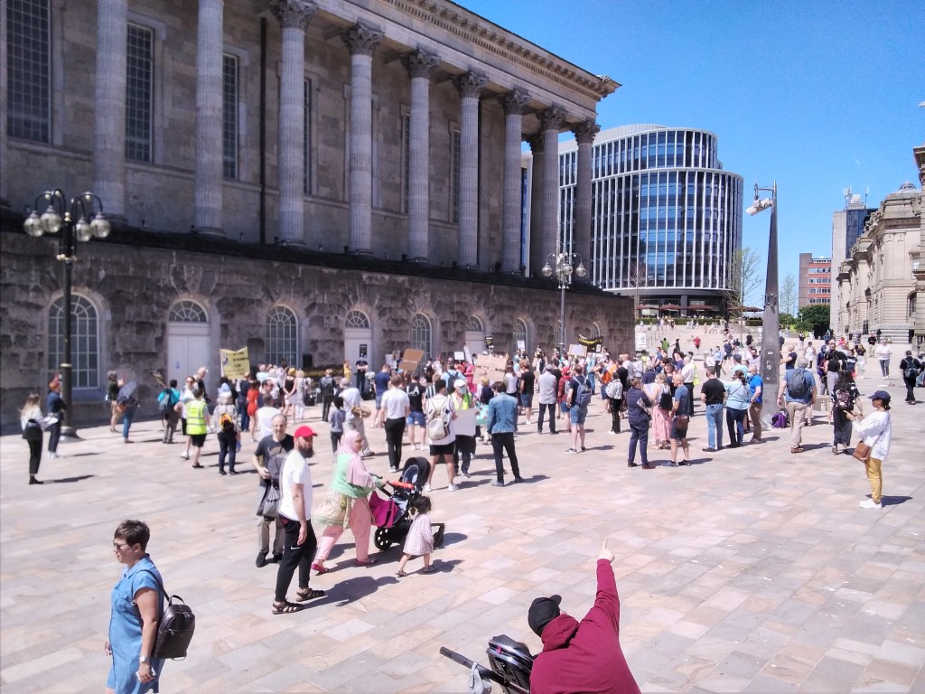 Protesters in Victoria Square, Birmingham. It is a sunny day.
