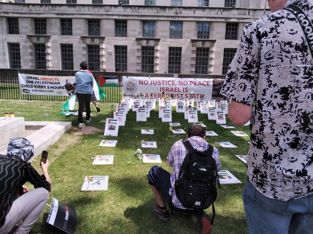 Cardboard signs representing graves of Palestinians killed by Israel, in background sign reading "No Justice No Peace Israel is a Terrorist State'