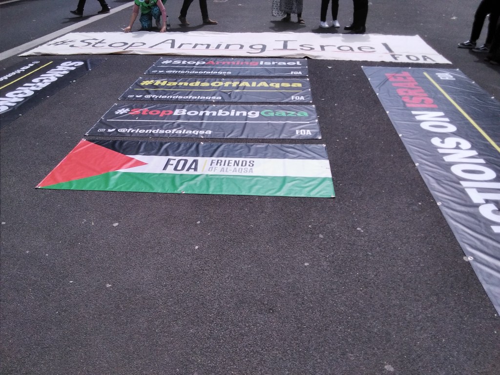 Signs reading Stop Arming Israel, Hands of Al Aqsa, Stop Bombing Gaza, FOA Friends of Al Aqsa
