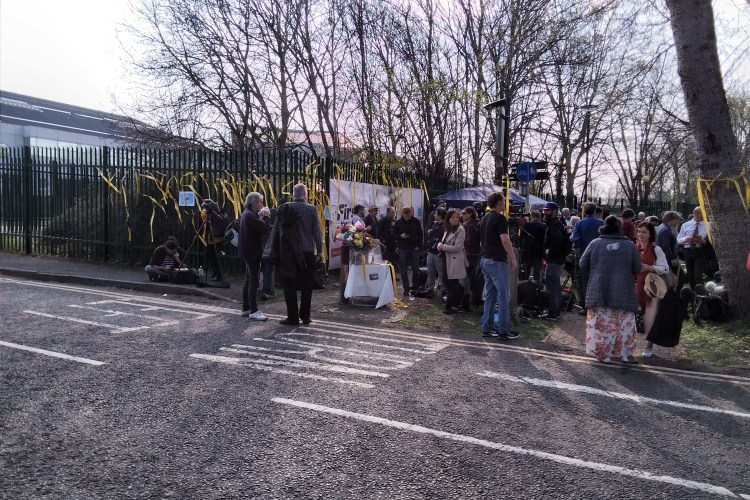 Protesters outside Belmarsh Prison. Yellow ribbons are tied to the fence and trees.