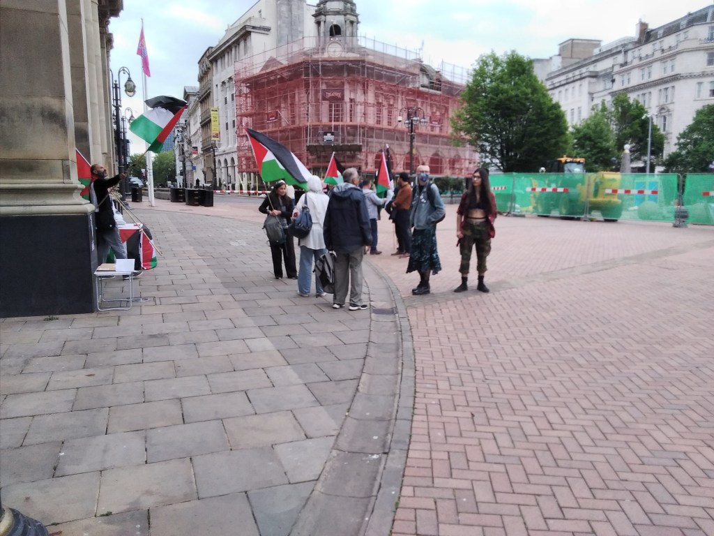 Small number of Palestine protesters in Victoria Square. One man on the left stands waving a flag .