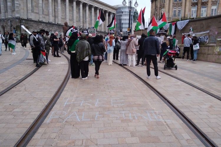 Palestine protesters standing on tram lines in Birmingham City Centre. Multiple flags are being waved.