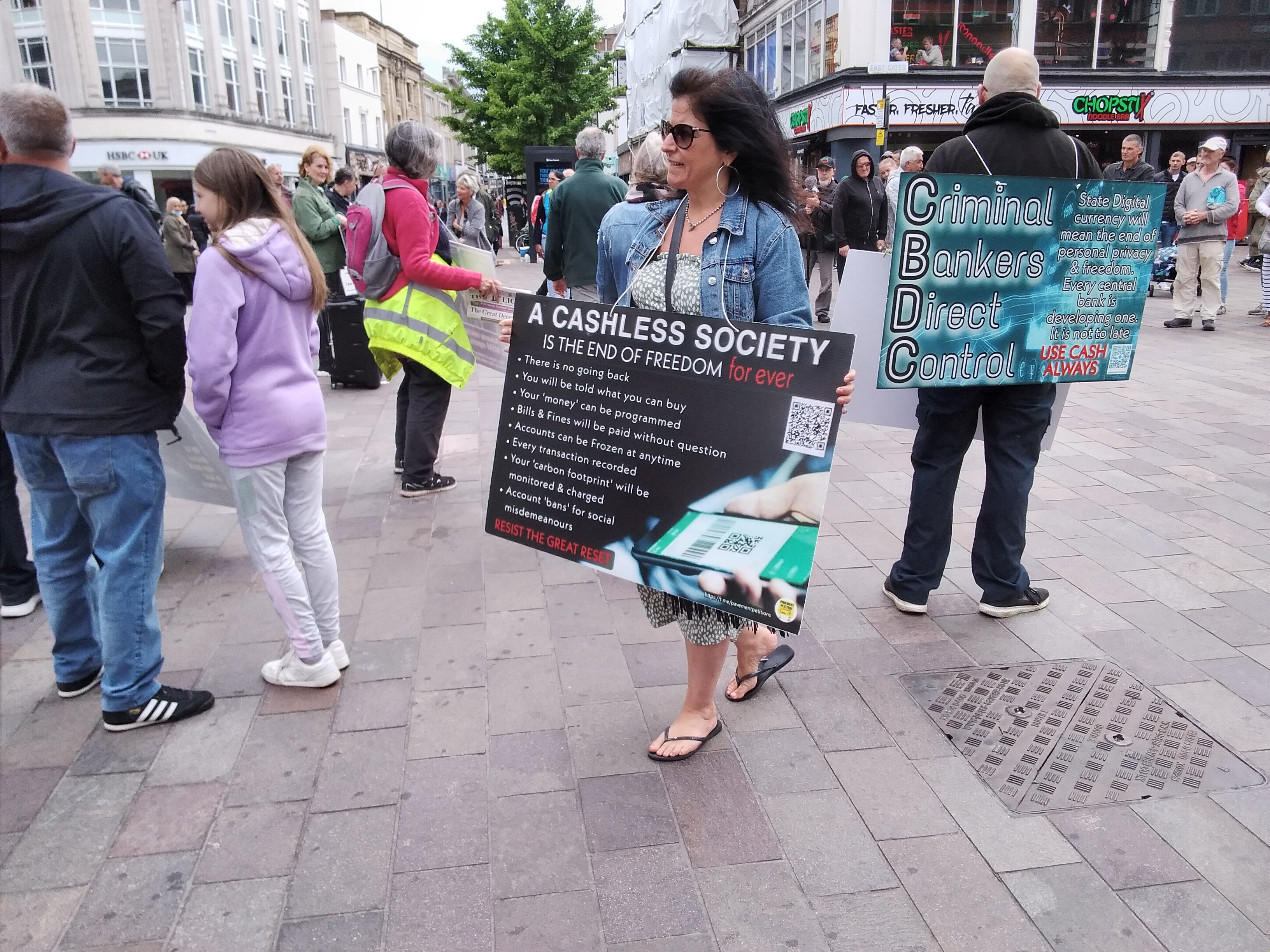 Woman holding sign reading 'A Cashless Society is the End of Freedom For Ever - Resist the Great Reset'