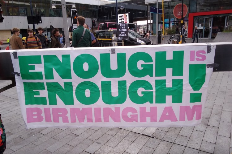 Banner reading Enough Is Enough Birmingham. Sign in the background reads 'End the Siege on Gaza'.