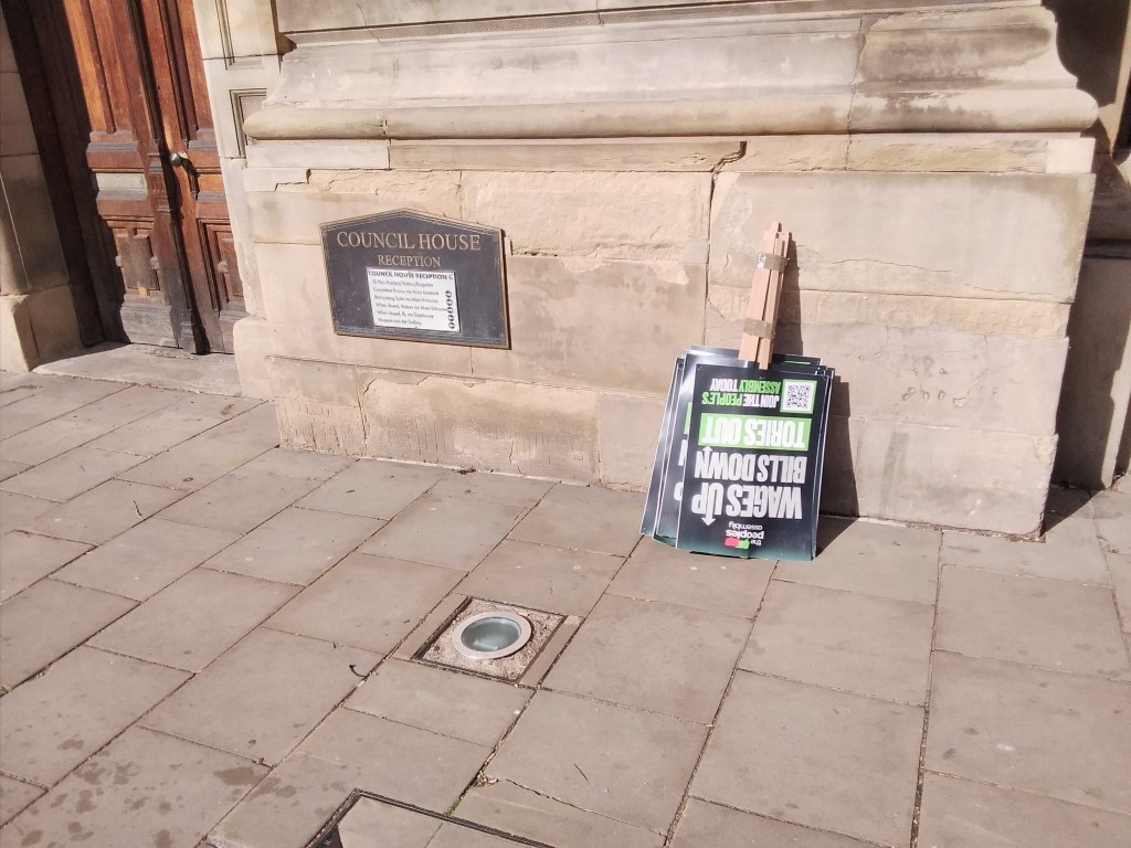 Signs leaning against a wall upside down reading 'Wages Up Bills Down Tories Out'