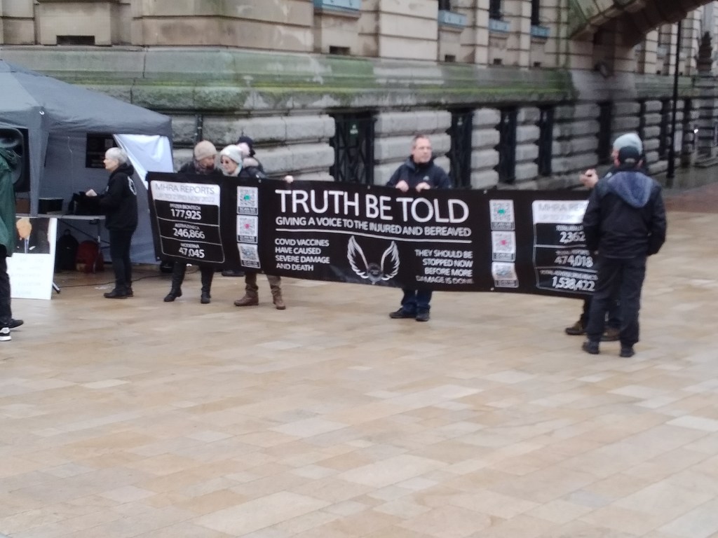 Multiple people holding a large banner saying 'Truth be Told: Giving a Voice to the Injured and Bereaved'