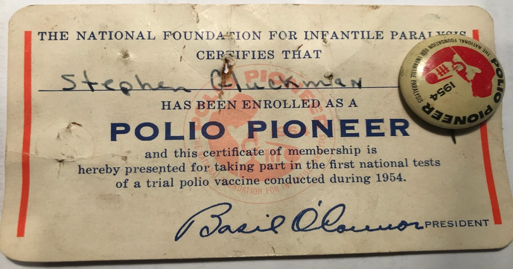 Image shows a worn certificate with the text: "The National Foundation for Infantile Paralysis Certifies that Stephen Gluckman has been enrolled as a Polio Pioneer and this certificate of membership is hereby presented for taking part in the first national tests of a trial polio vaccine conducted during 1954. Basil O'Connor, President. The image also displays a badge with the text Polio Pioneer 1954 The National Foundation for Infantile Paralysis.