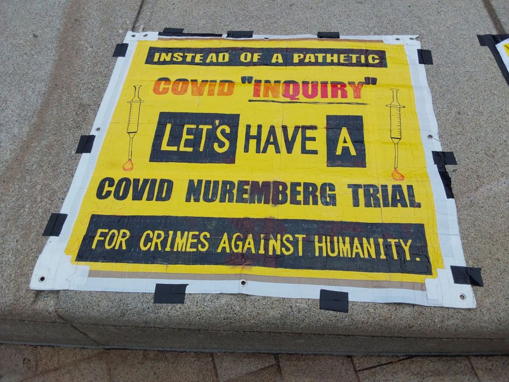 Sign taped to a step reading Instead of a pathetic Covid inquiry, let's have a covid nurenberg trial for crimes against humanity