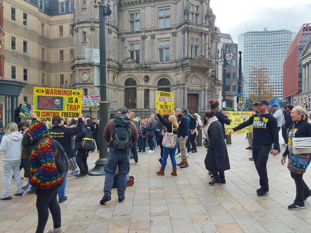 Protesters marching against Brit Card holding yellow signs. Sign reads Warning Brit Card is a trap to control freedom