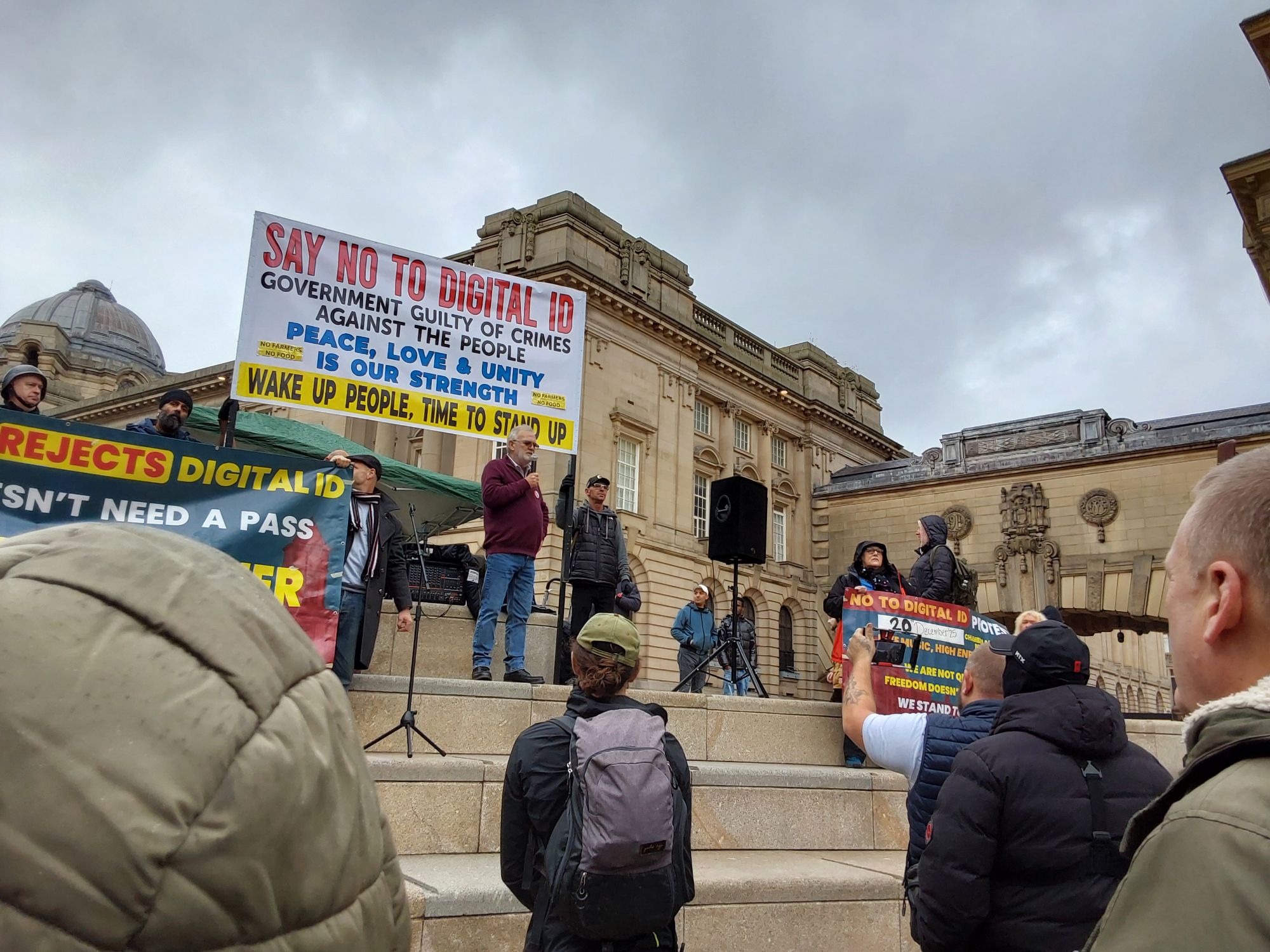 Man in a maroon shirt stands in front of a banner reading 'Say No to Digital ID'